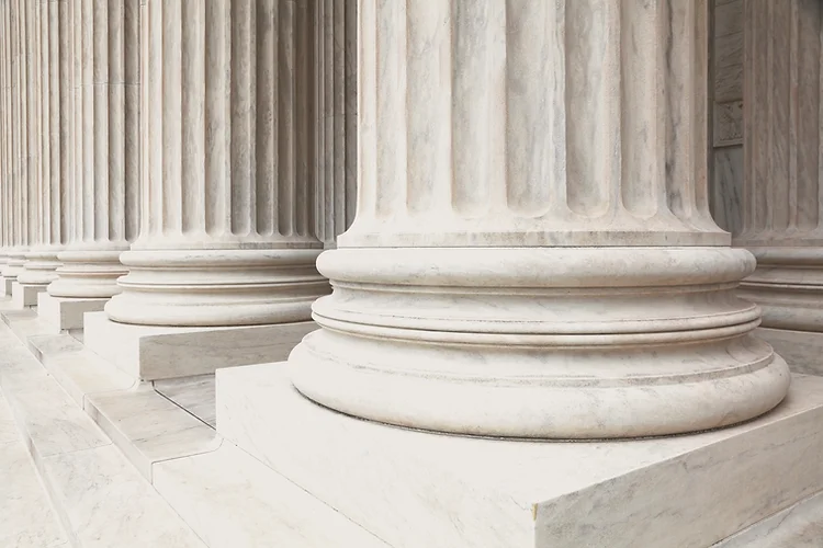Close-up of classical stone columns with fluted detailing, in neutral beige and gray tones, conveying a formal, solemn mood